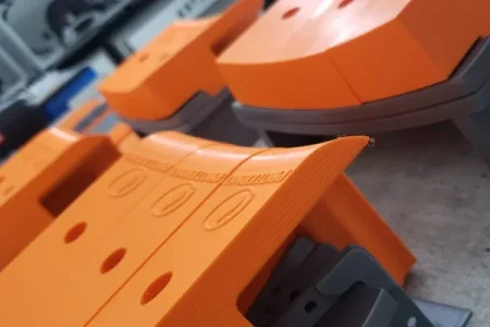 Peça industrial em impressão 3D na cor laranja, desenvolvida para aplicação técnica em ambiente industrial.